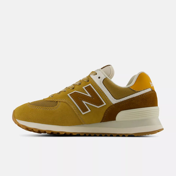 A pair of New Balance 574 sneakers in a mustard yellow and beige colorway,  on a light gray background.