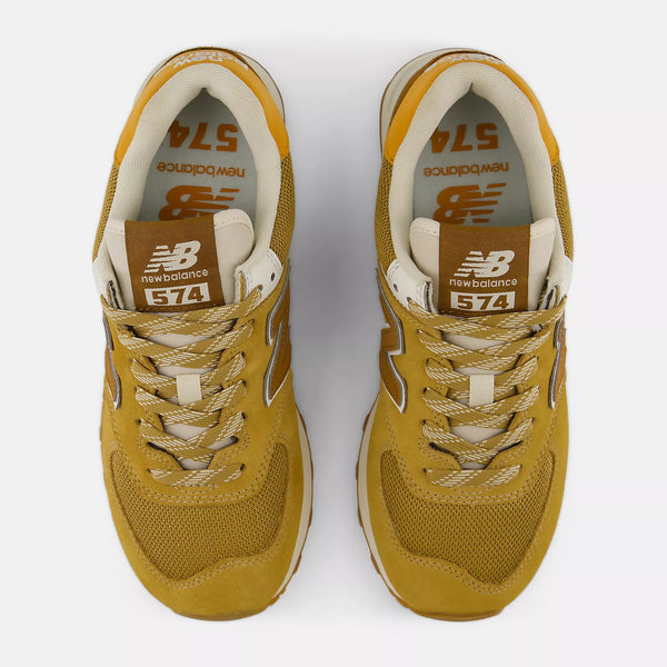 A pair of New Balance 574 sneakers in a mustard yellow and beige colorway,  on a light gray background.