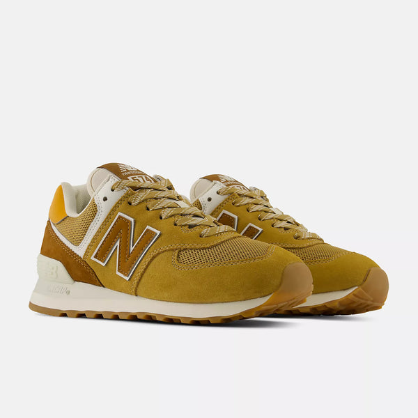 A pair of New Balance 574 sneakers in a mustard yellow and beige colorway,  on a light gray background.