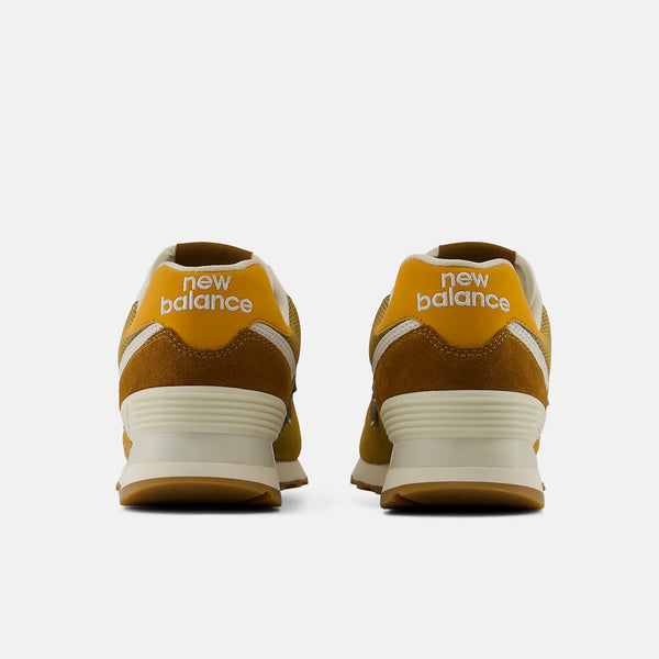 A pair of New Balance 574 sneakers in a mustard yellow and beige colorway,  on a light gray background.