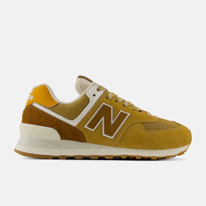 A pair of New Balance 574 sneakers in a mustard yellow and beige colorway,  on a light gray background.