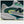 Gray and green NB athletic shoe with brand logo on a dark background
